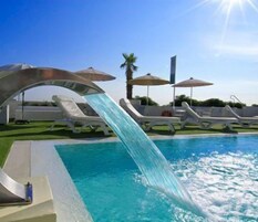 Una piscina al aire libre, sombrillas, sillones reclinables de piscina