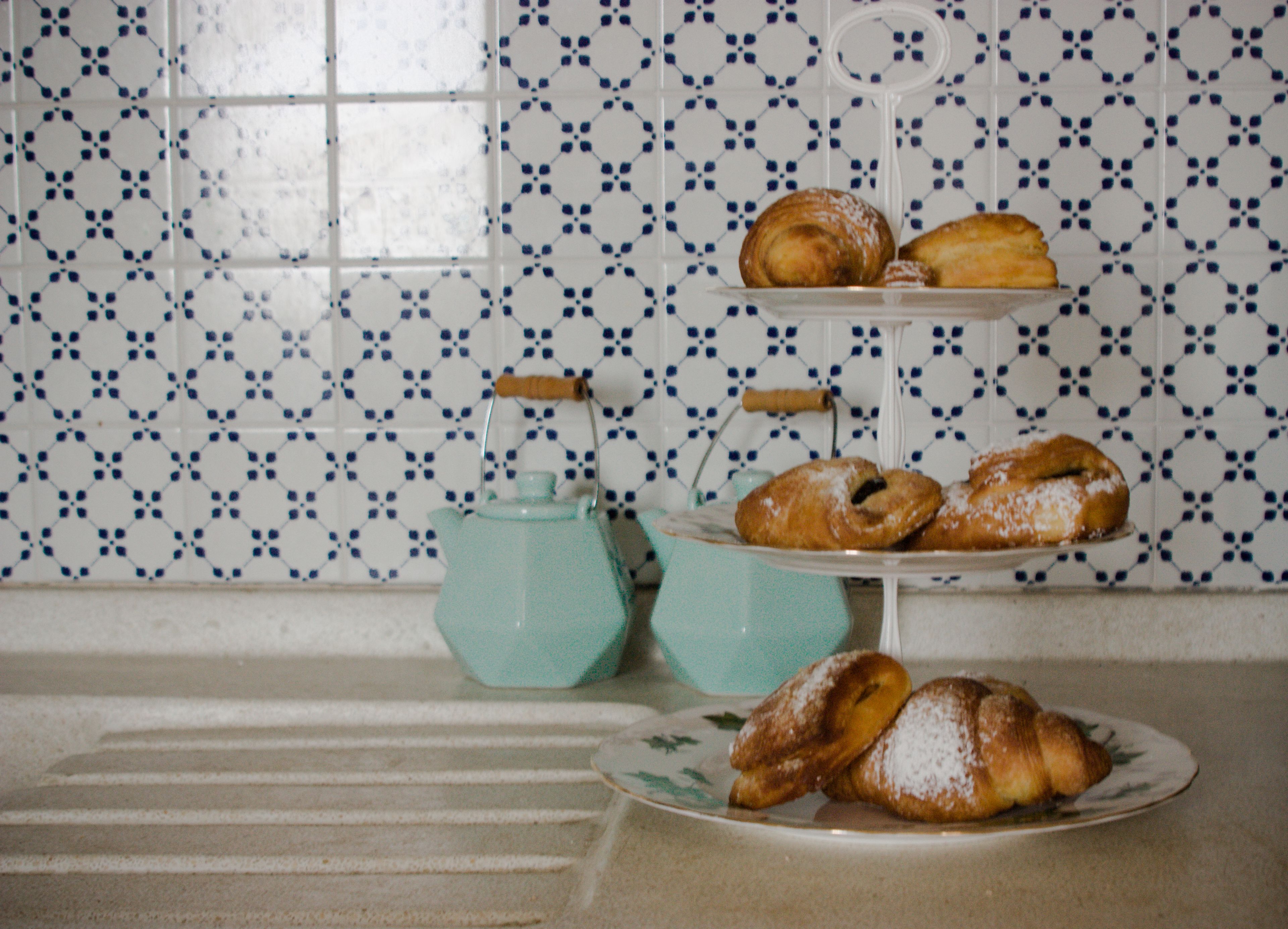 Une cuisine avec un mur recouvert de carreaux, une bouilloire turquoise et une assiette remplie de pâtisseries.