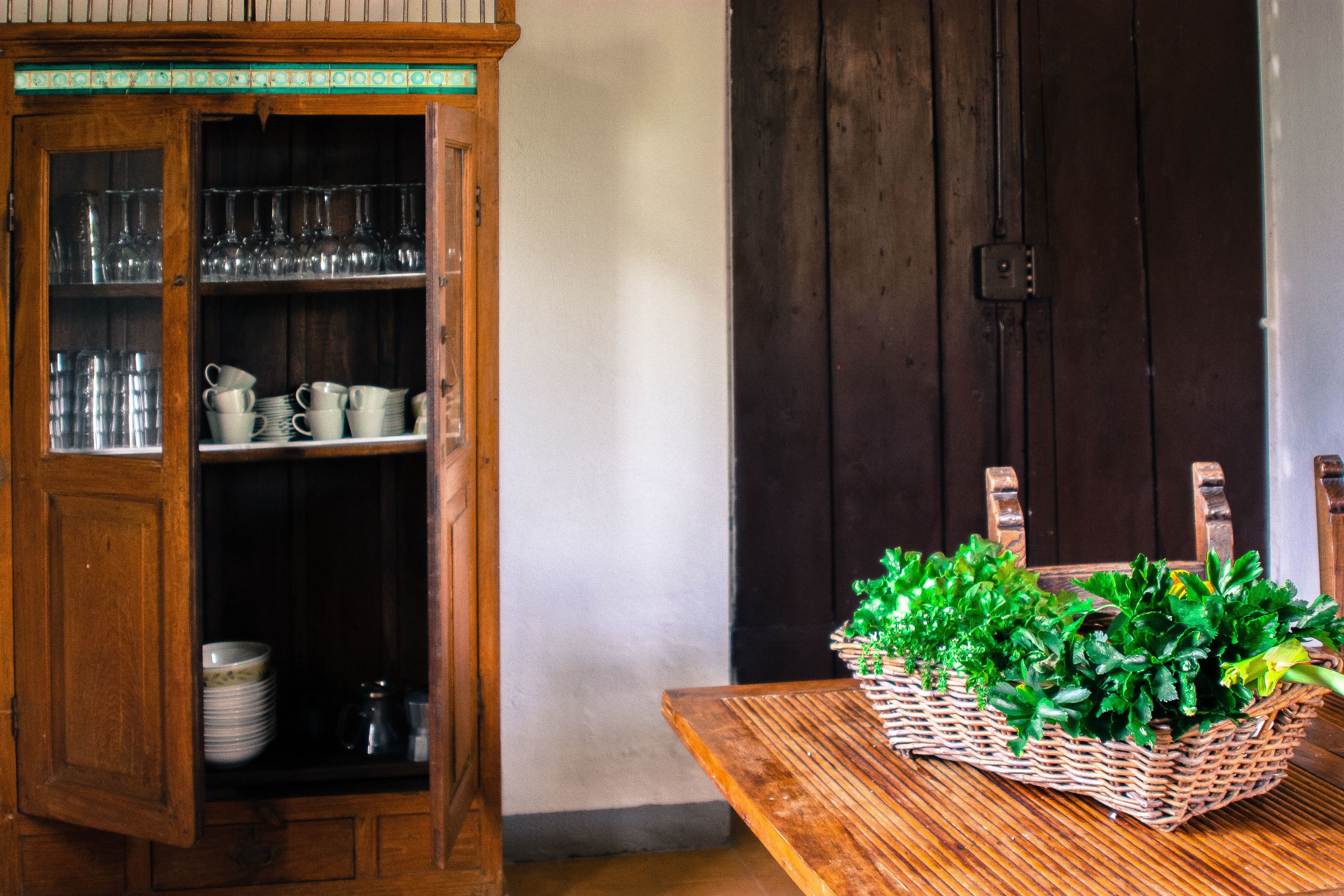 Un meuble en bois contenant de la verrerie et un panier en osier rempli de verdure, le tout posé sur une table en bois.