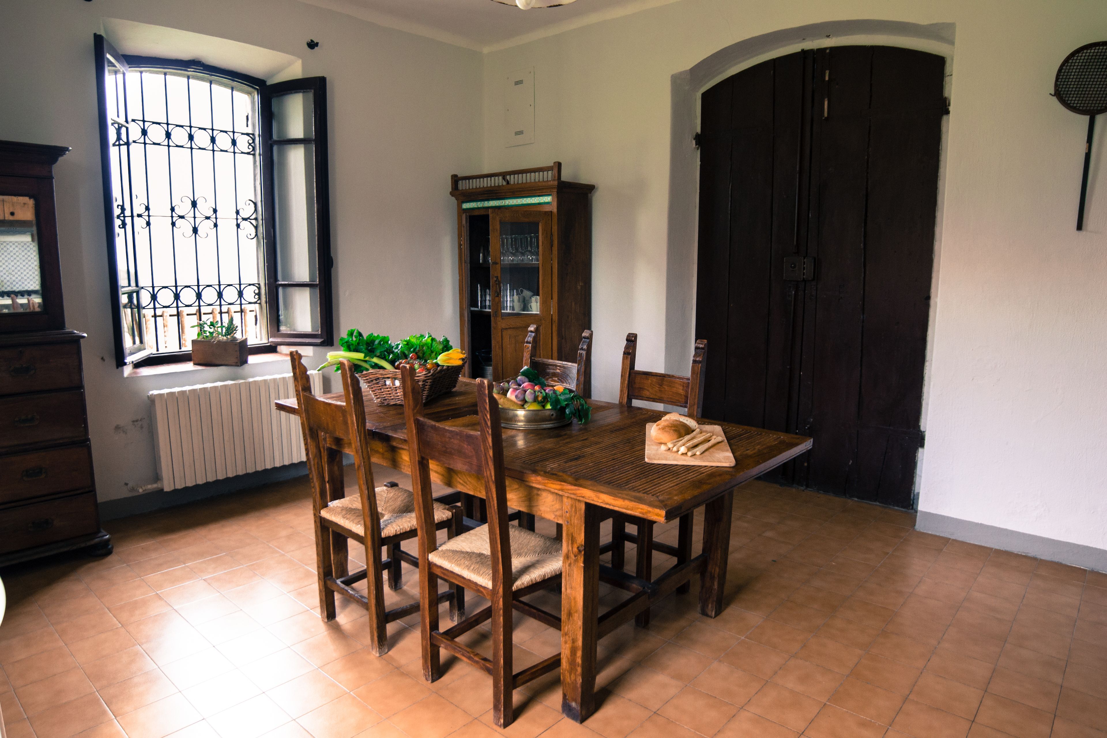 A dining area with a wooden table and chairs, a cabinet with glass doors, and a window with metal bars.