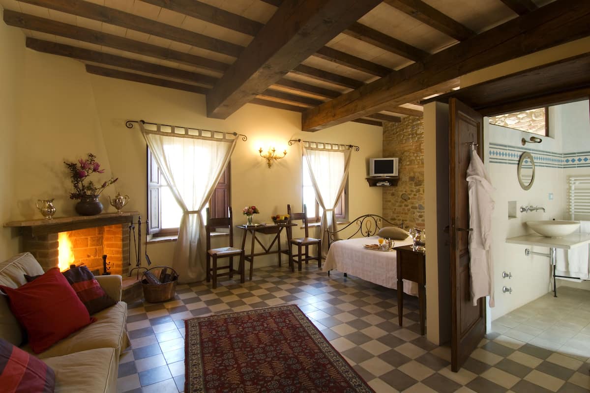 Una habitación acogedora con chimenea, piso de cuadros, una cama, una mesa con sillas y un baño con lavamanos y espejo.
