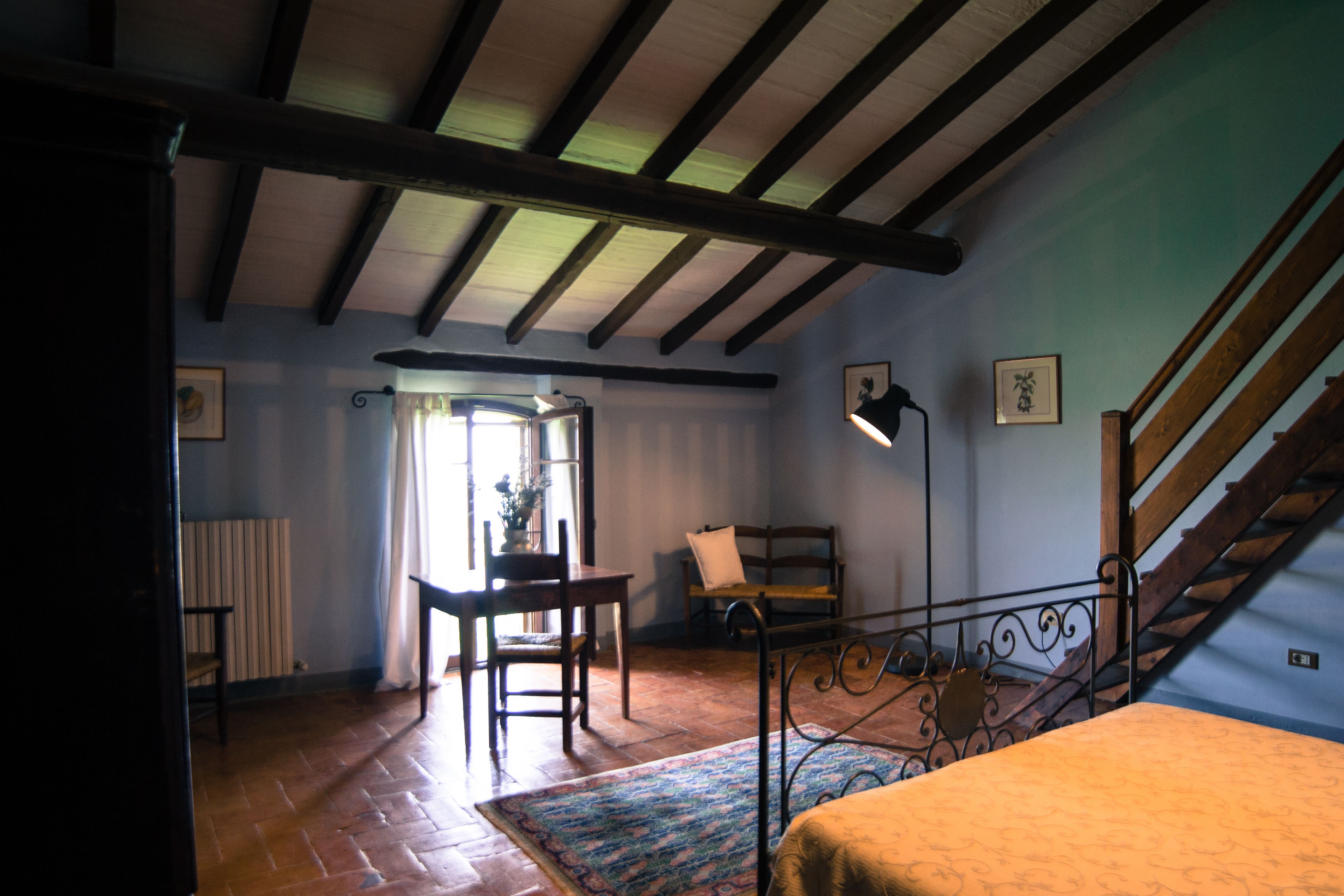 A room with a bed, a chair, a table, and a staircase.