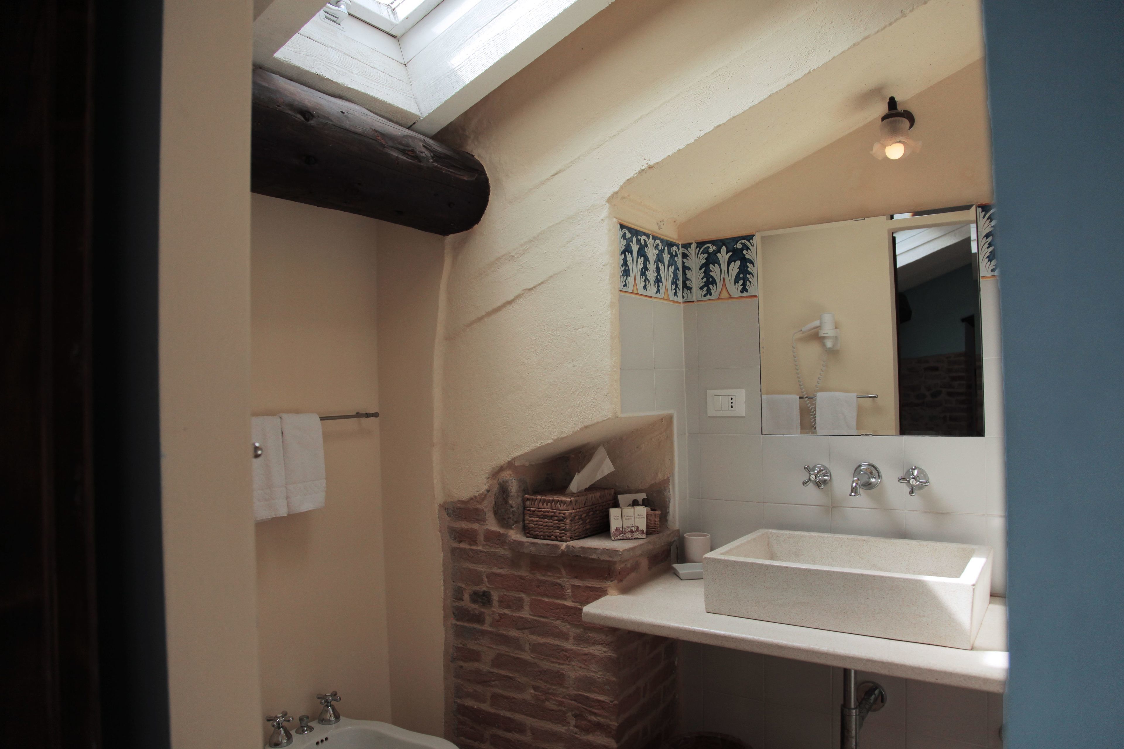 A bathroom with a skylight, a white sink, a mirror, and a brick wall.