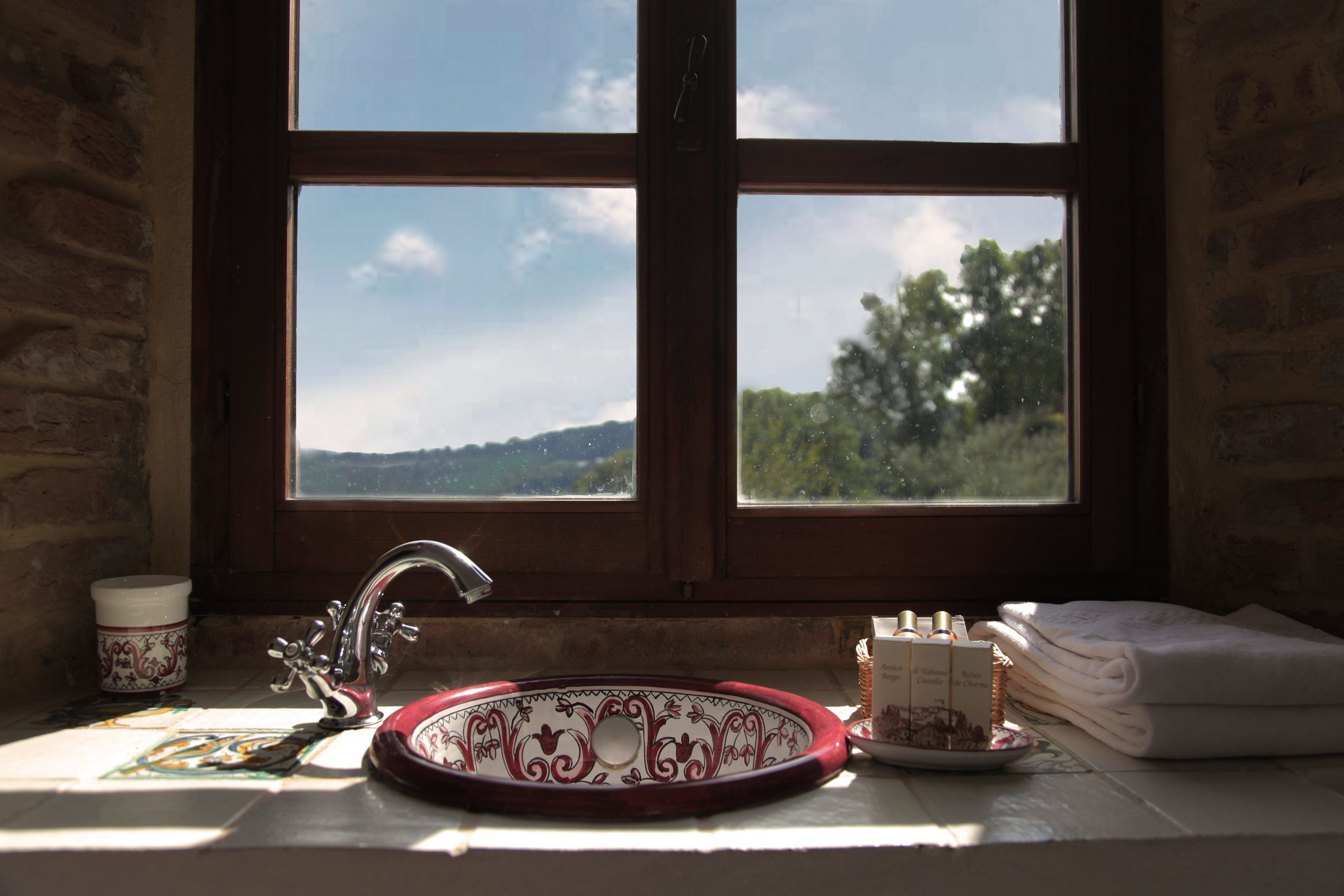 Ein Badezimmer mit Waschbecken, einem Fenster mit Blick auf Bäume und Hügel sowie einem Handtuchhalter mit gefalteten Handtüchern.