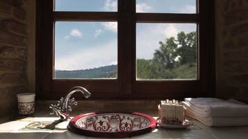 Ein Badezimmer mit Waschbecken, einem Fenster mit Blick auf Bäume und Hügel sowie einem Handtuchhalter mit gefalteten Handtüchern.