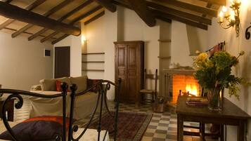 A cozy room with a checkered floor, a bed with a metal frame, a wooden cabinet, a fireplace, and a table with a vase of flowers.