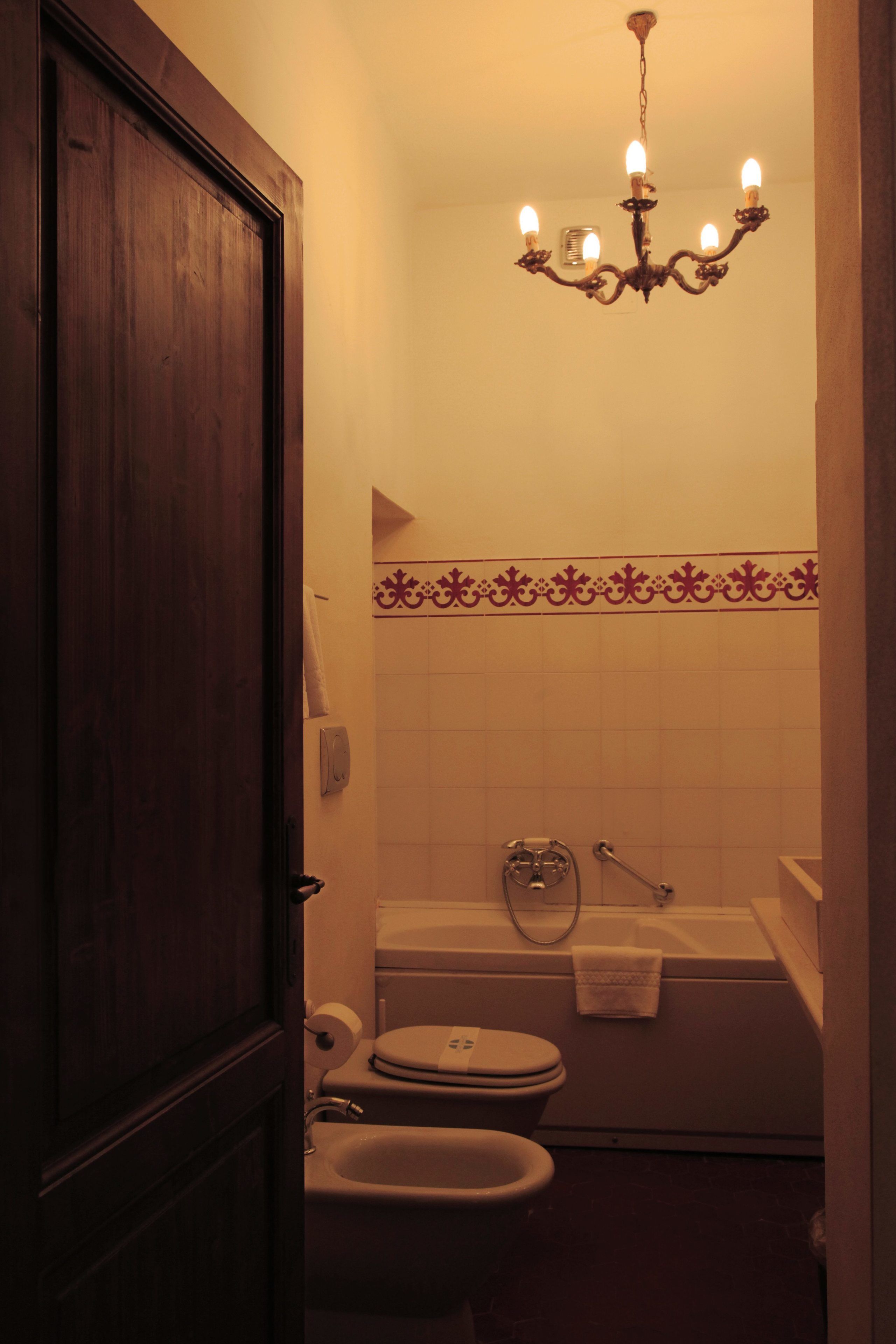 Un baño con puerta de madera, una bañera blanca, un inodoro blanco, un bidé y una araña.