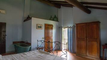 A bedroom with a bed, a wooden wardrobe, a wooden door, a green bathtub, and a window with curtains.