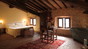 Un dormitorio con cama, una silla de madera, una mesa con un florero, una pared de piedra y una bañera antigua.