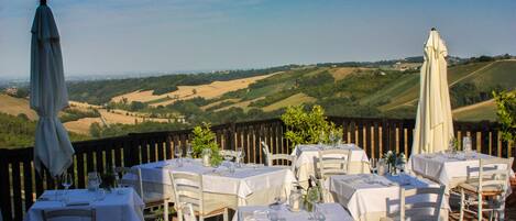 Un área de comedor al aire libre con mesas dispuestas para una comida, con vistas a un paisaje pintoresco.
