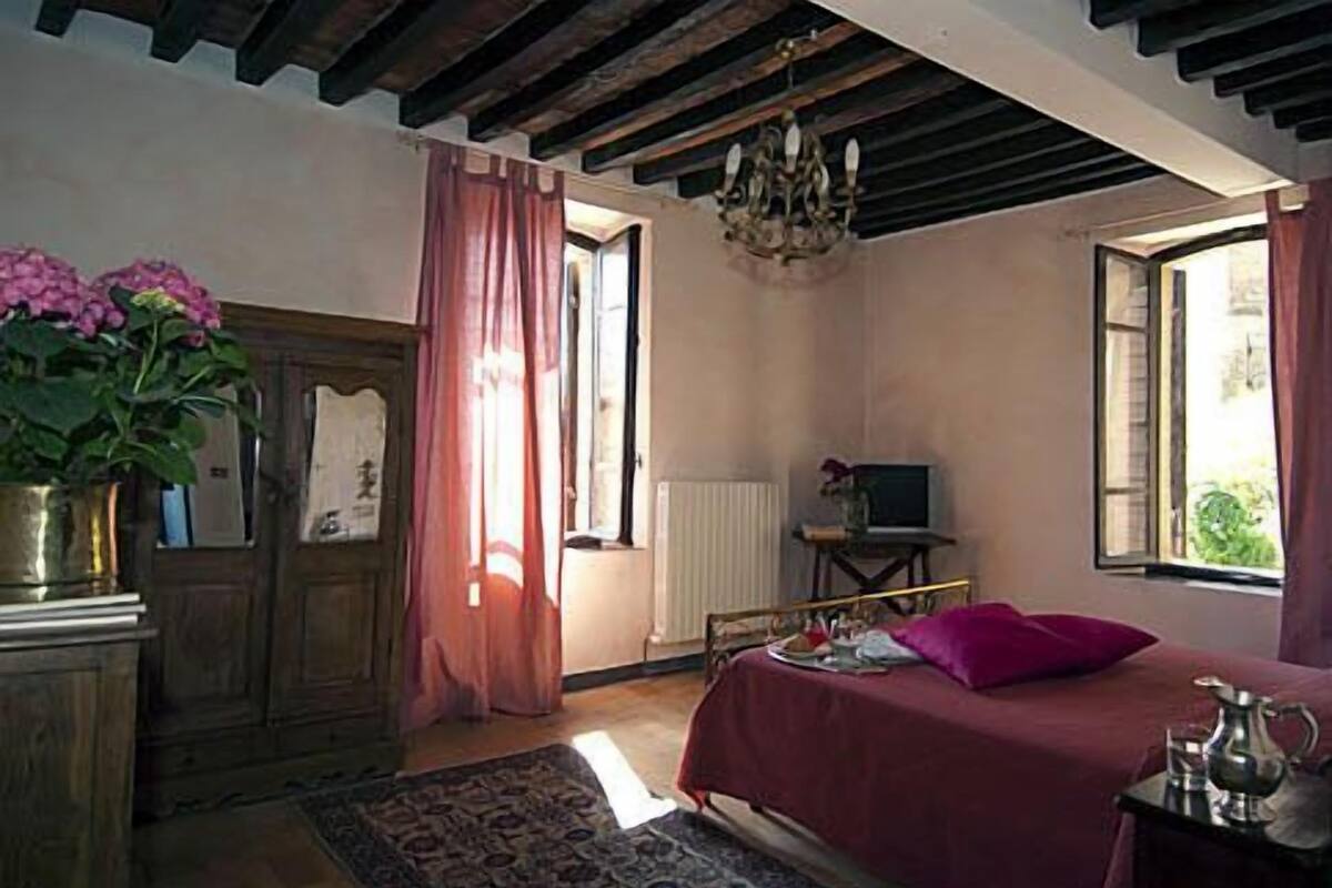 Un dormitorio con cama, televisor, radiador y ventana con cortinas.