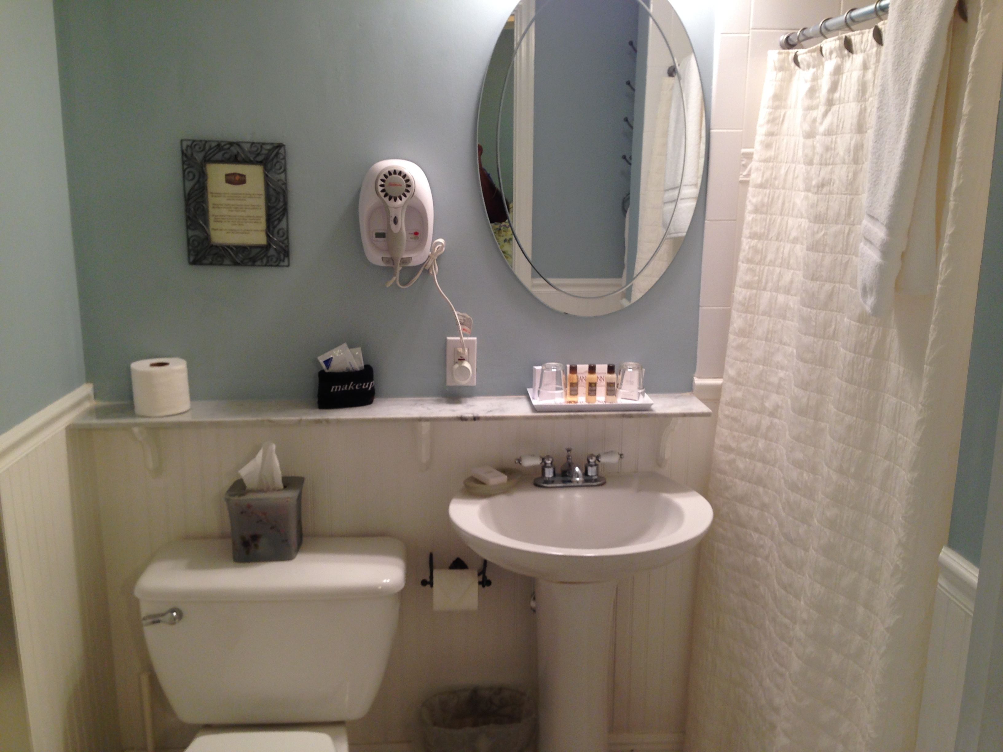 Ein Badezimmer mit Toilette, Waschbecken und Spiegel. Darüber befindet sich ein Handtuchhalter und an der Wand ein gerahmtes Zertifikat.