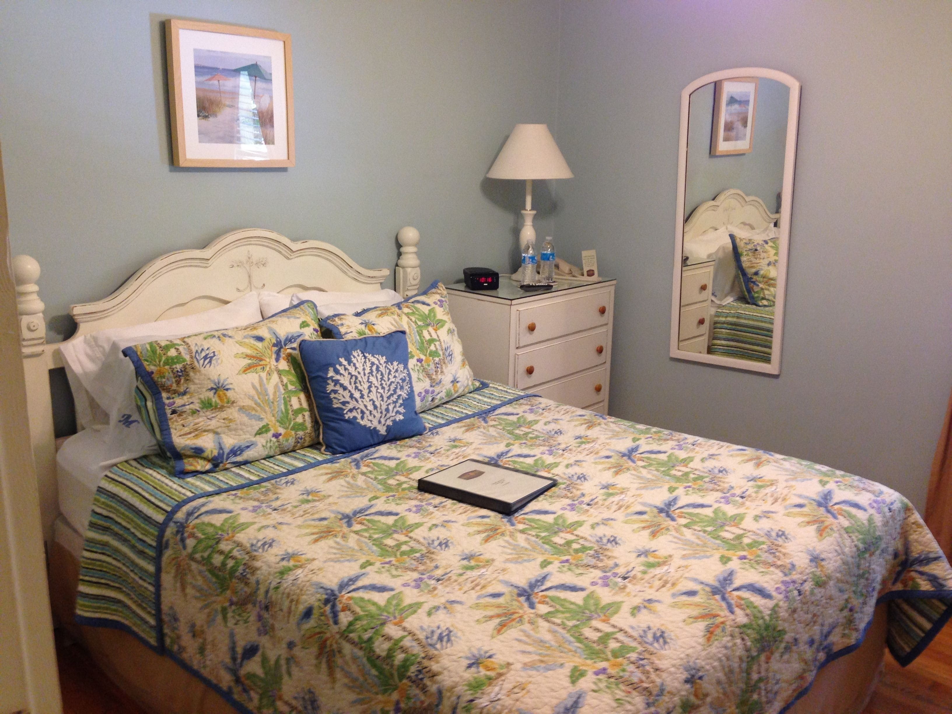 A neatly made bed with floral bedding, a bedside table with a lamp, and a mirror on the wall.