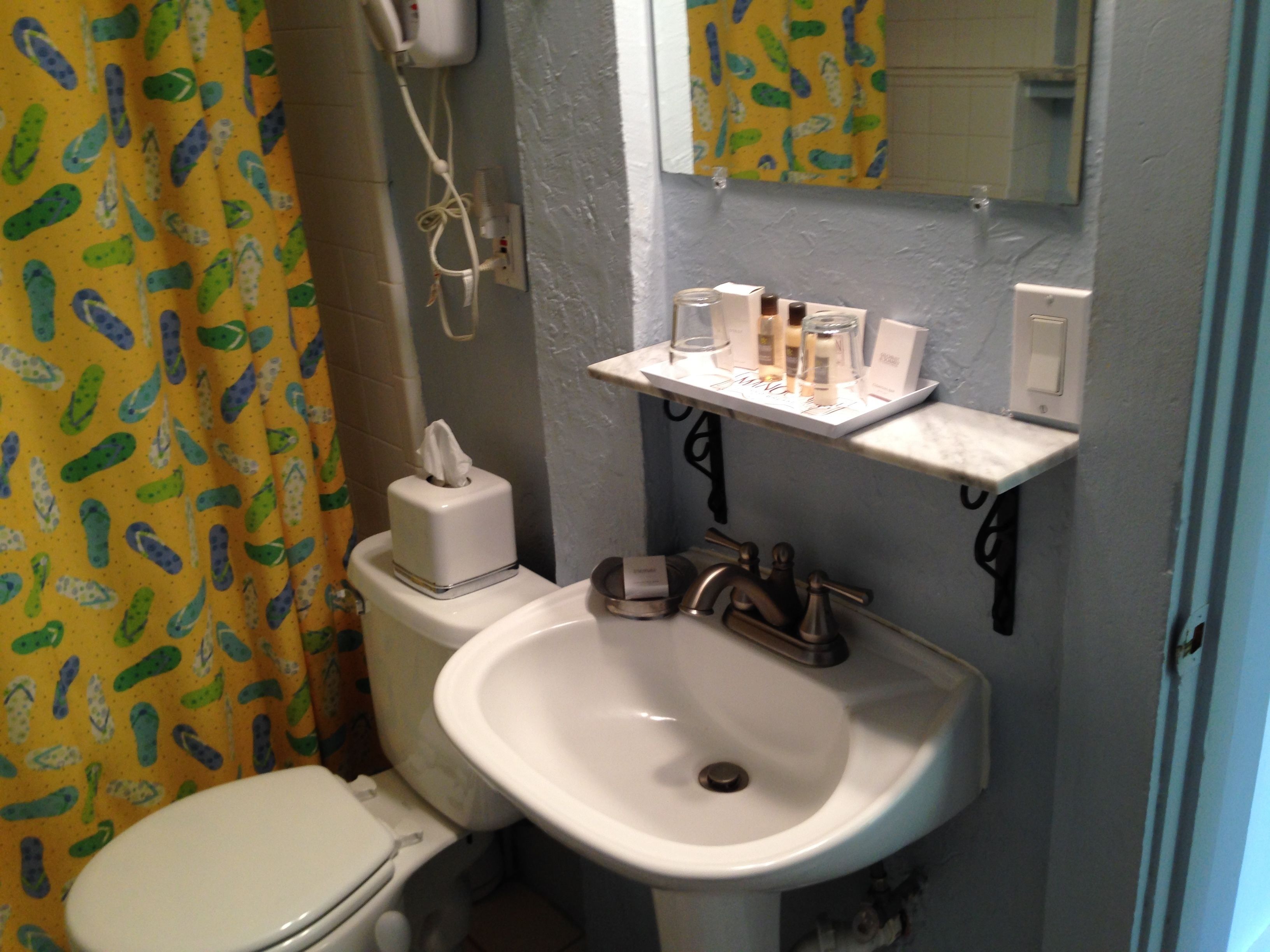 Un baño con inodoro, lavabo y estante con artículos de aseo.