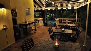 An outdoor patio with tables and chairs, a pool, and a covered area with string lights. - The Mango Inn Bed & Breakfast (Lake Worth)