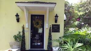 A yellow building with a black door, a sign reading "Mango Inn circa 1915", and a brick entrance. - The Mango Inn Bed & Breakfast (Lake Worth)