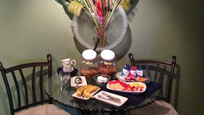 A dining table with a variety of food items, a decorative vase with flowers, and two jars of jam. - The Mango Inn Bed & Breakfast (Lake Worth)