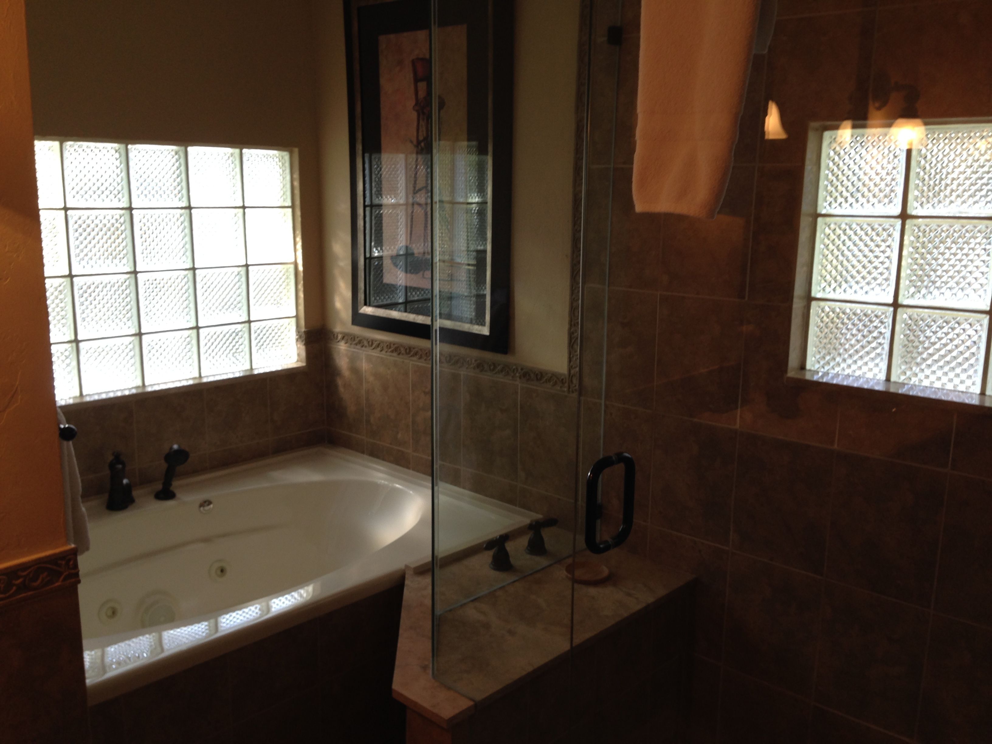 Une salle de bain avec une baignoire, une cabine de douche en verre et une fenêtre ornée d’une grille décorative.