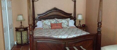 A four-poster bed with a wooden frame and a headboard with a curved design. There are two bedside tables with lamps on either side of the bed.