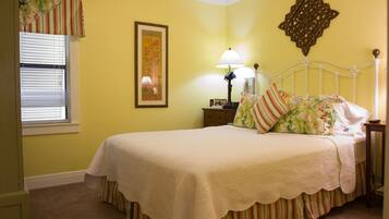 A bedroom with a bed, a nightstand, a lamp, a window with blinds, and a wall decoration.