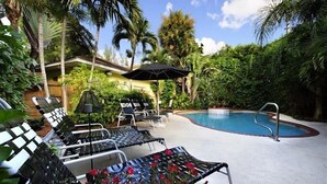 A pool area with lounge chairs, a pool, and surrounding greenery. - The Mango Inn Bed & Breakfast (Lake Worth)