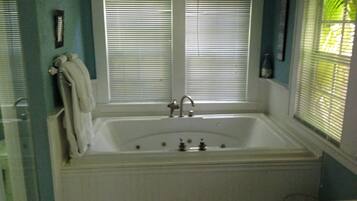 Ein Badezimmer mit einer weißen Badewanne, zwei Jalousiewindosen, einem Handtuchhalter und einer Toilette.