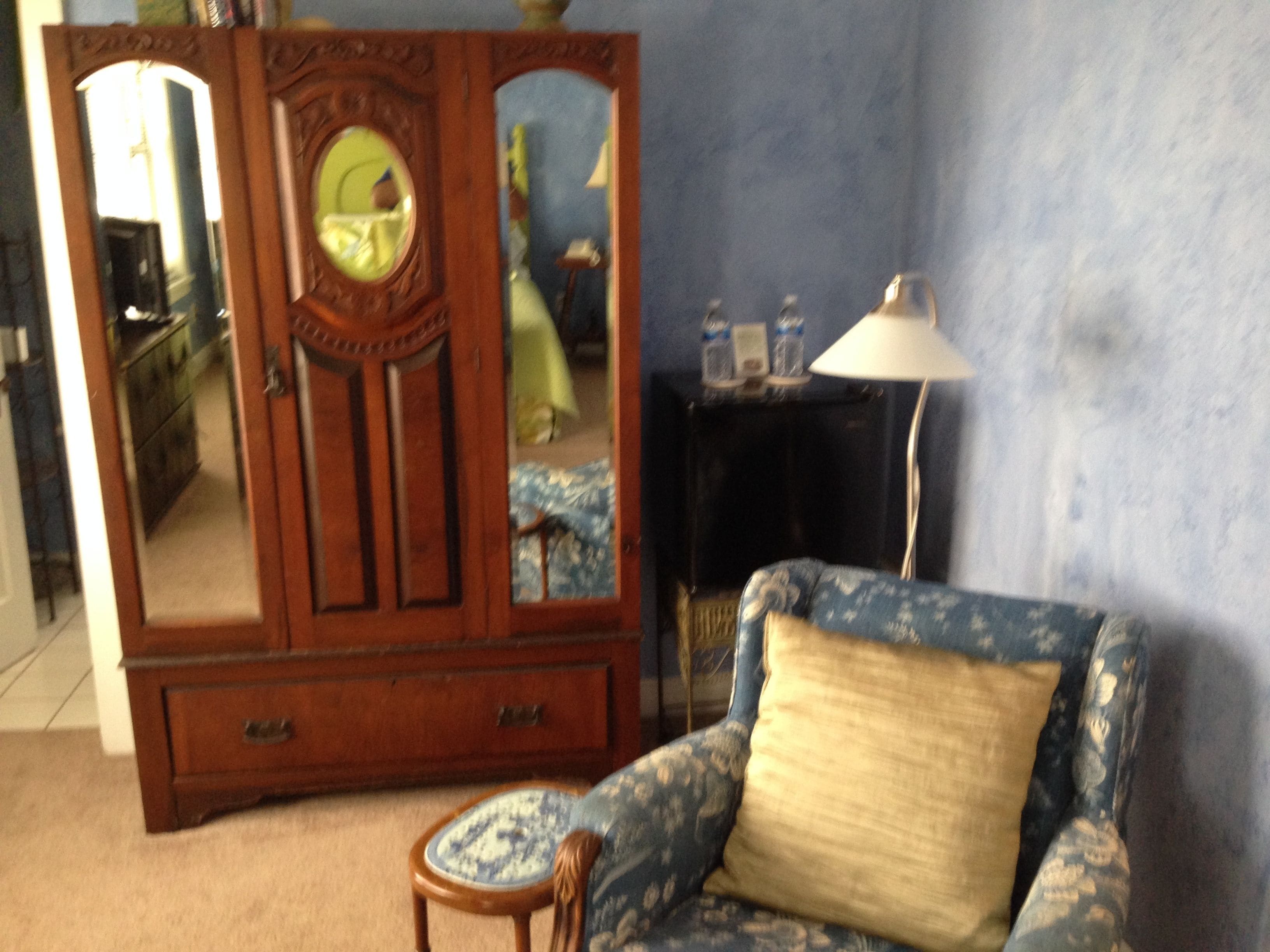 A room with a wooden armoire, a patterned sofa, a small round table, and a lamp.