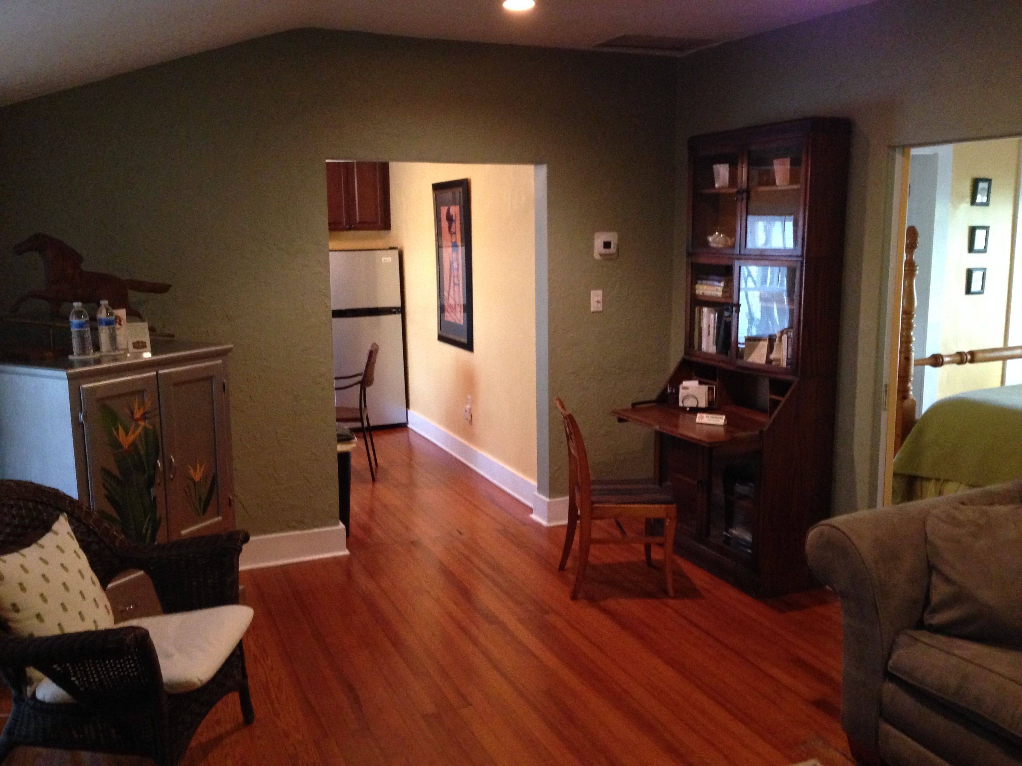 A living room with hardwood floors, a dining area, and a kitchen visible through an open doorway.