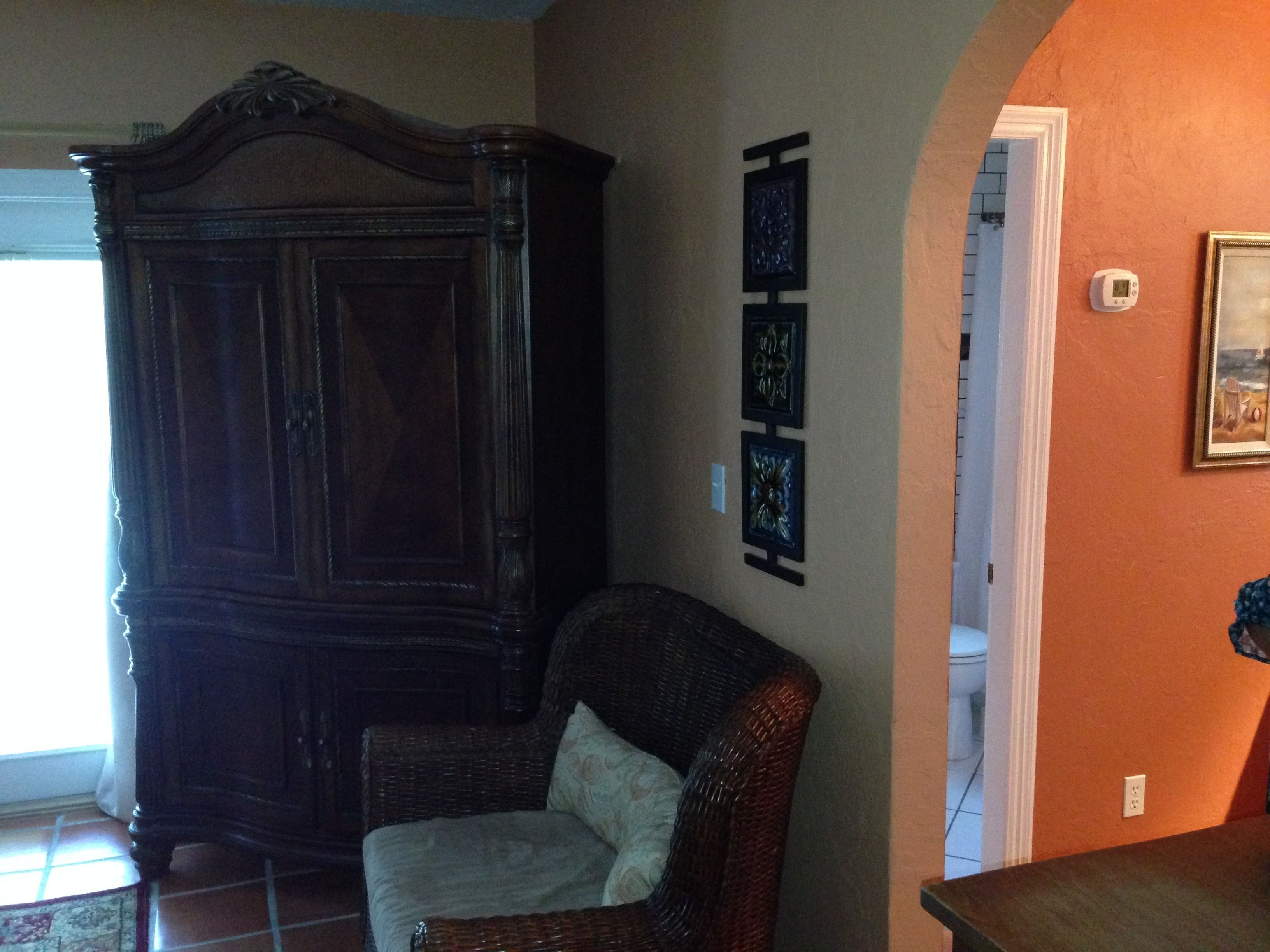 Una habitación con un mueble de madera oscura, una silla de mimbre y una pared con tres obras de arte enmarcadas.