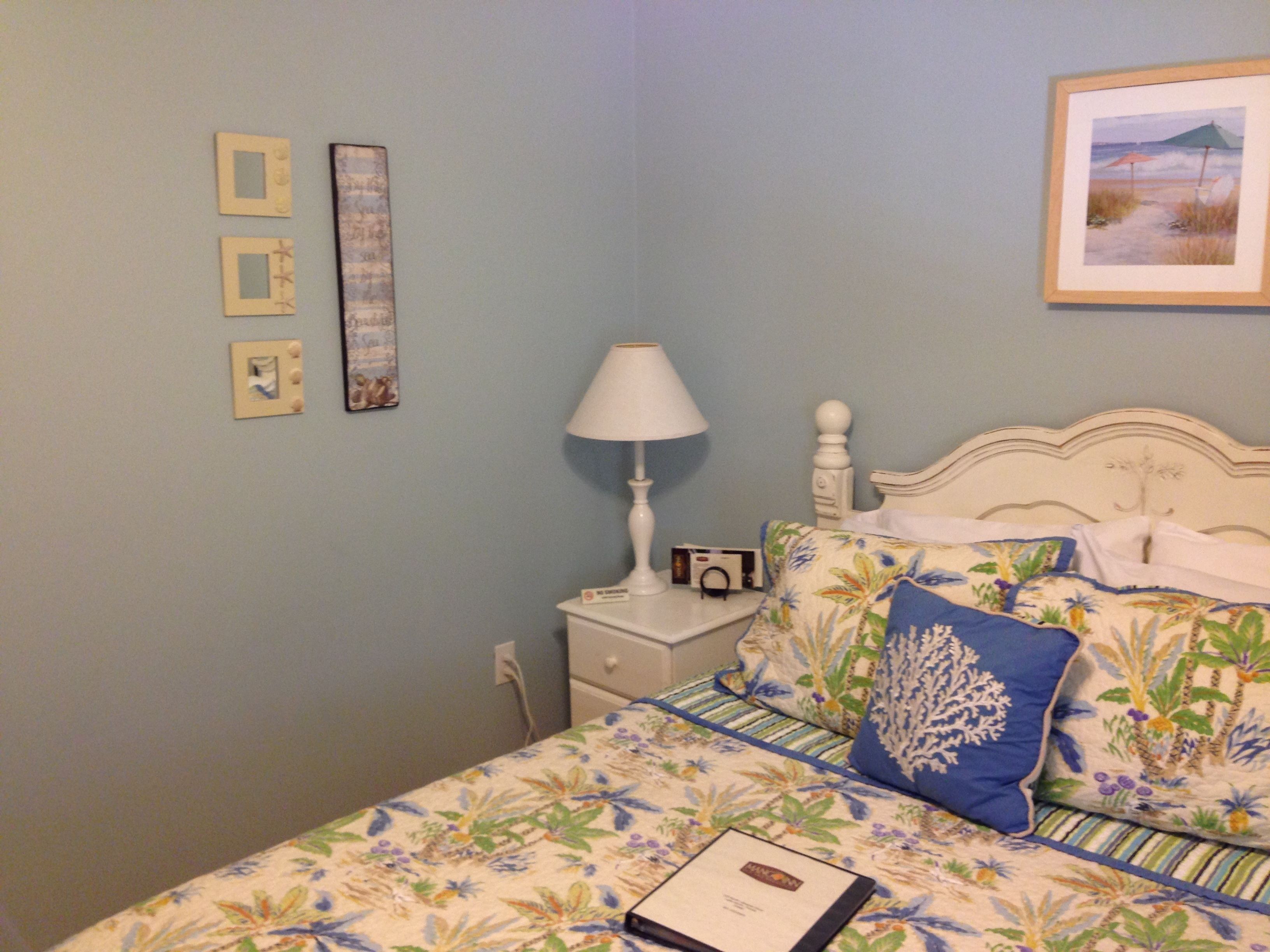 Un dormitorio con una cama, una mesita de noche, una lámpara y un cuadro en la pared.