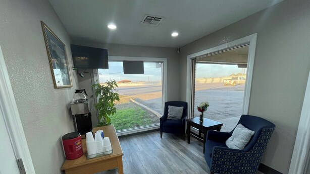 A room with a large window, a coffee machine, a table with a vase of flowers, and two chairs. - Regency Inn Hondo (Hondo)