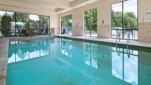 Une piscine intérieure avec des parois en verre transparent, une zone de terrasse carrelée et un poste de surveillance pour les sauveteurs.
