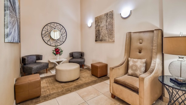 Un salon moderne avec un fauteuil beige, deux canapés gris, une petite table blanche et un miroir rond orné d’un motif d’arbre.