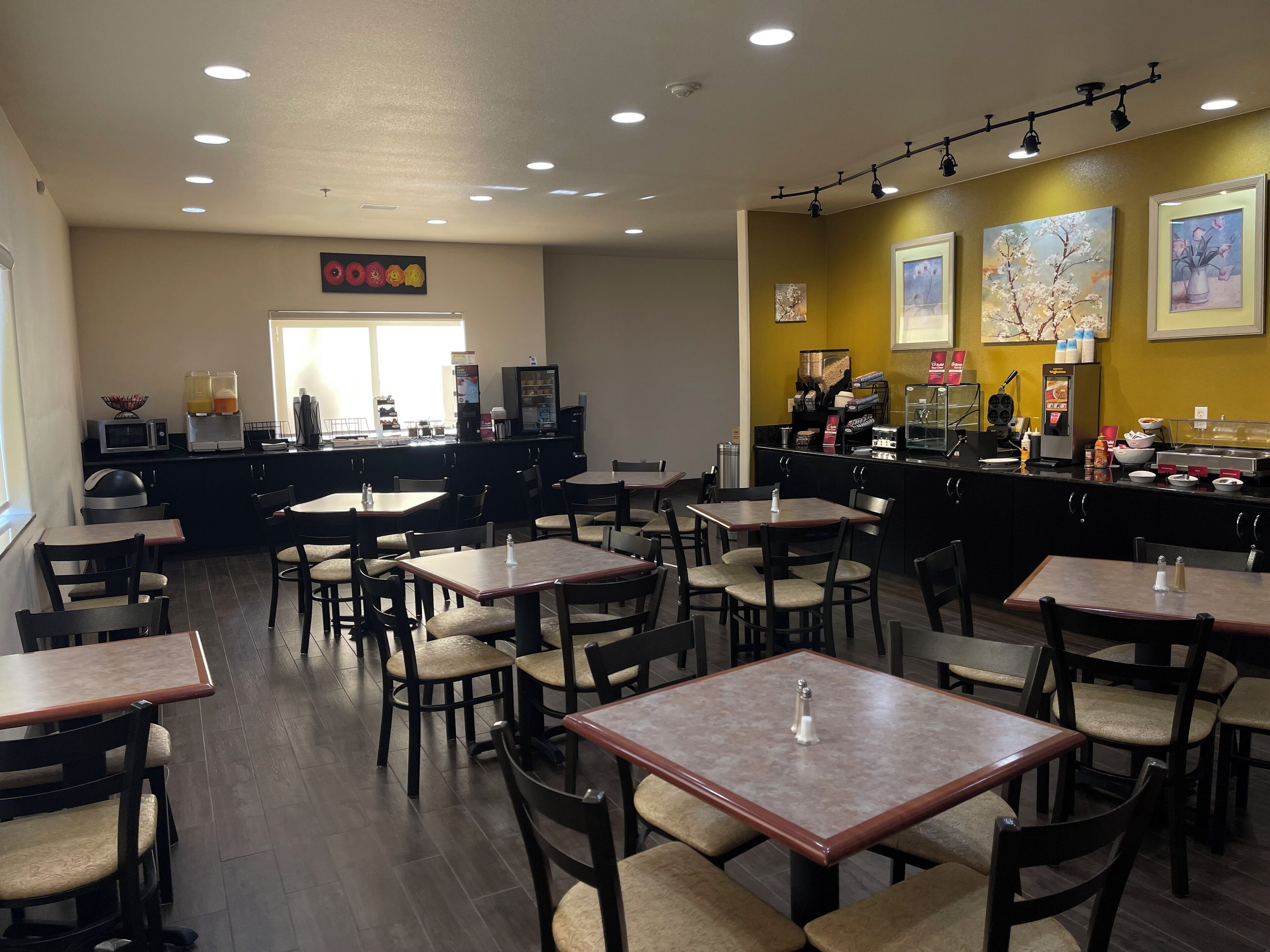 A restaurant with multiple tables and chairs, a counter with a coffee machine, and artwork on the walls.