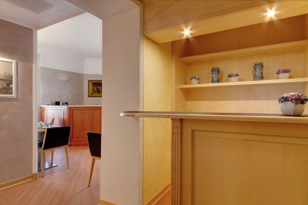 A modern kitchen with wooden cabinets, a dining area with two chairs, and decorative items on shelves.