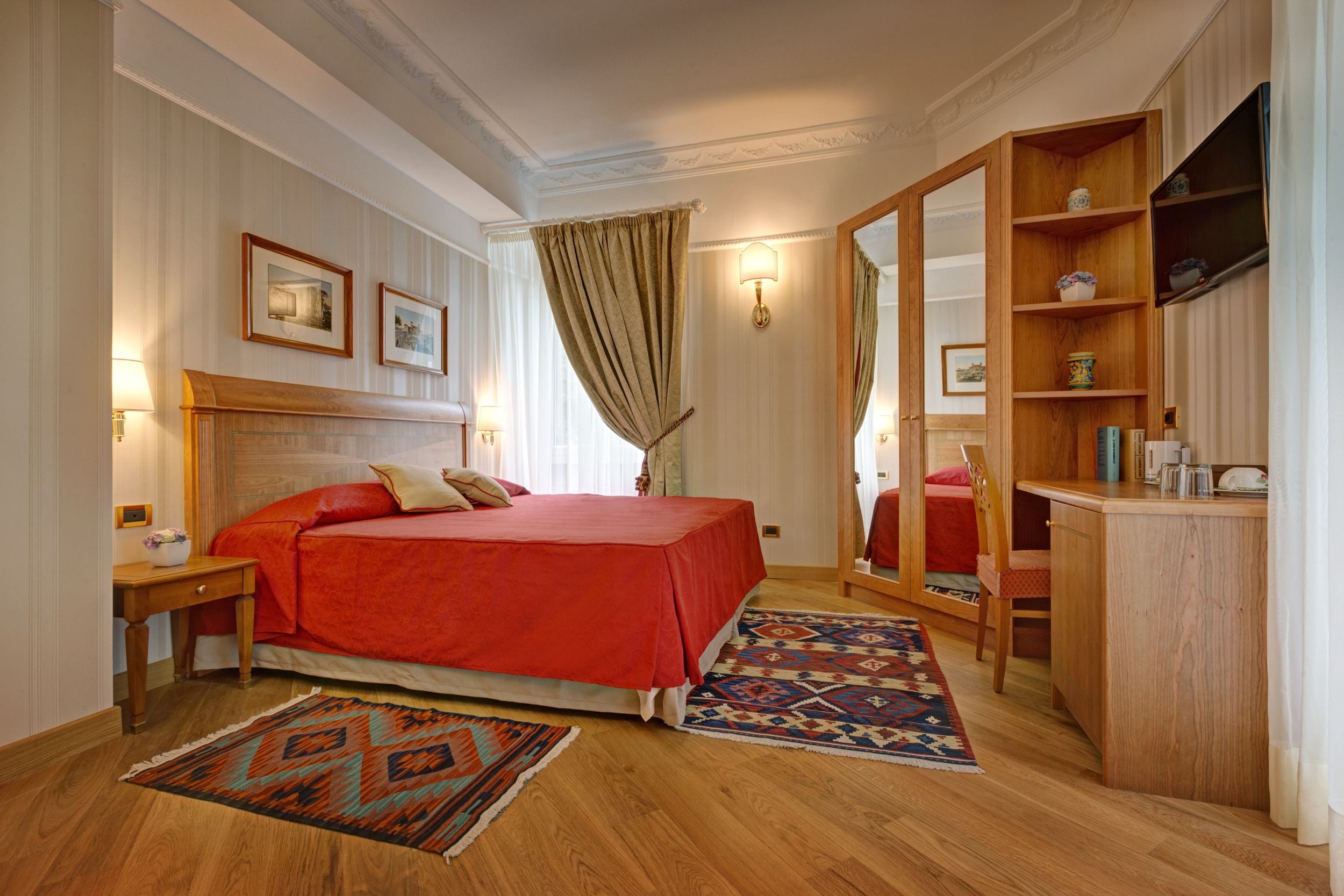 A hotel room with a large bed, a wooden desk, a mirror, and a bookshelf.