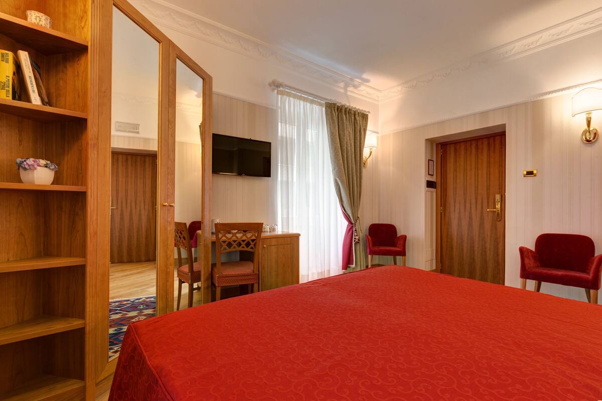 A hotel room with a large bed, wooden furniture, a television, and a wardrobe.