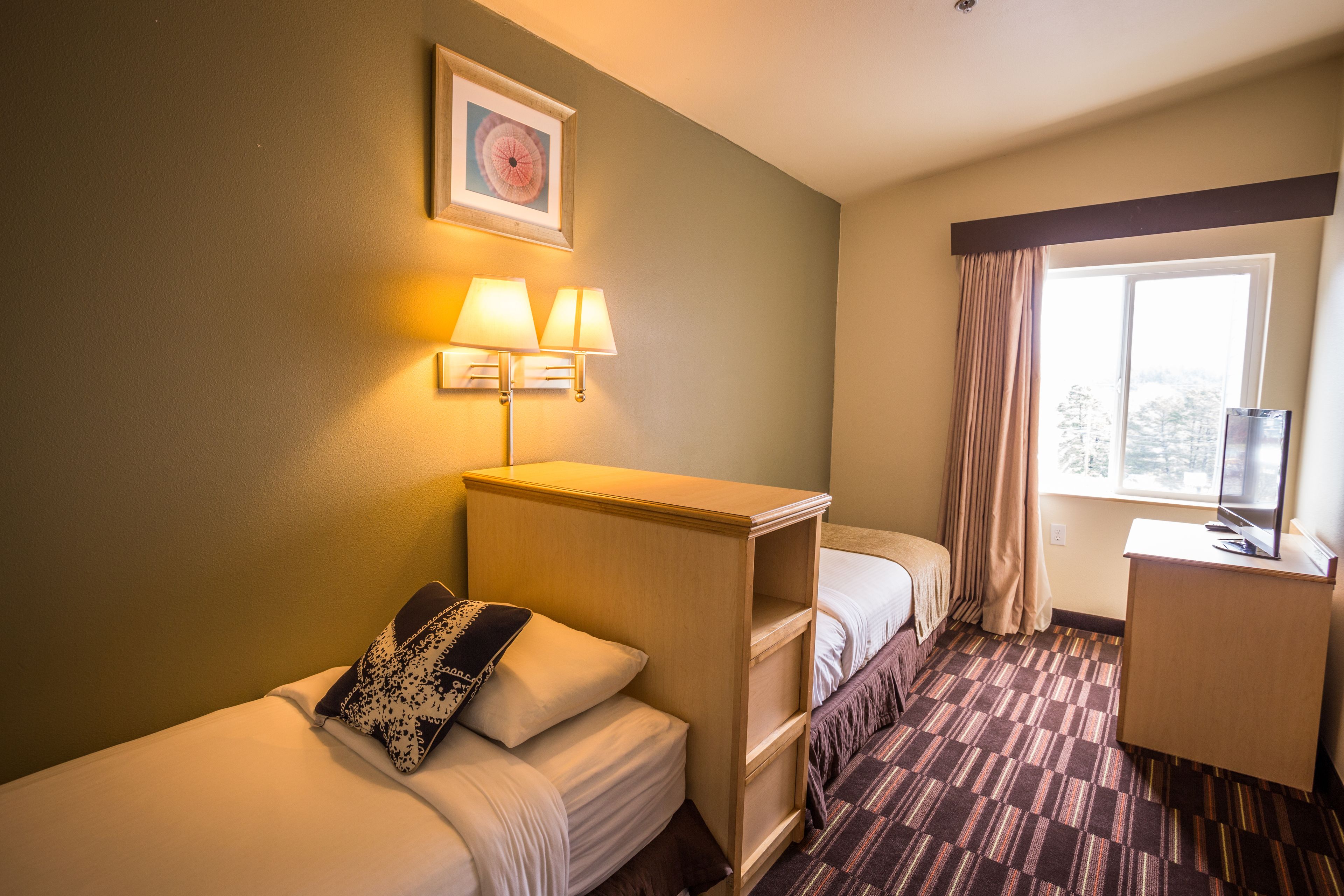 A hotel room with two beds, a desk, a television, and a window with curtains.