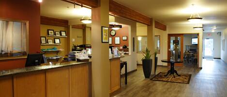 A reception area with a wooden reception desk, framed pictures on the wall, a clock, and a potted plant.