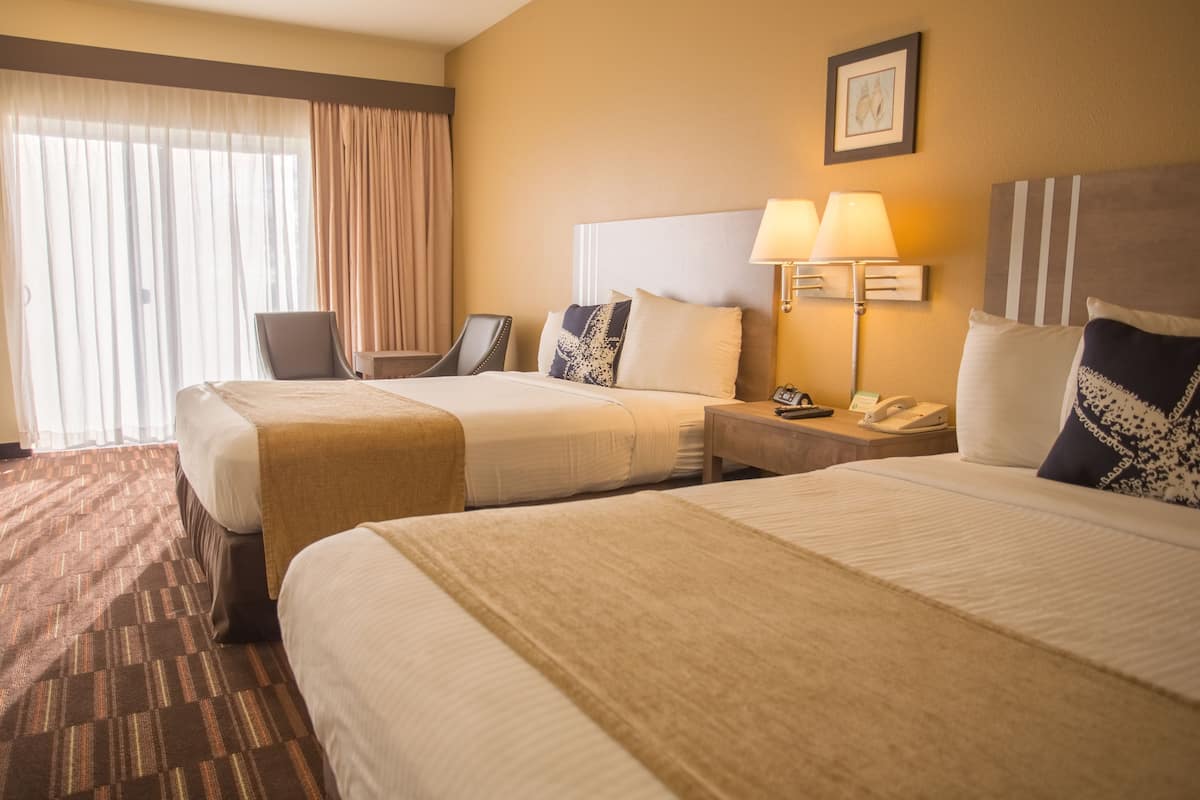 Ein Hotelzimmer mit zwei Betten, einem Schreibtisch, einem Stuhl, einer Lampe und einem Telefon.