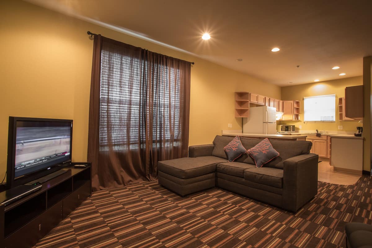 Ein Wohnzimmer mit einem Ecksofa, einem Flachbildfernseher und einer Küche im Hintergrund.