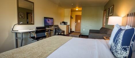 Una habitación de hotel con cama, escritorio, computadora, televisor y sofá.
