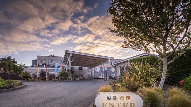 L’entrée d’un hôtel, agrémentée d’une enseigne indiquant « ENTRÉE », est entourée d’espaces paysagers et d’une allée couverte.
