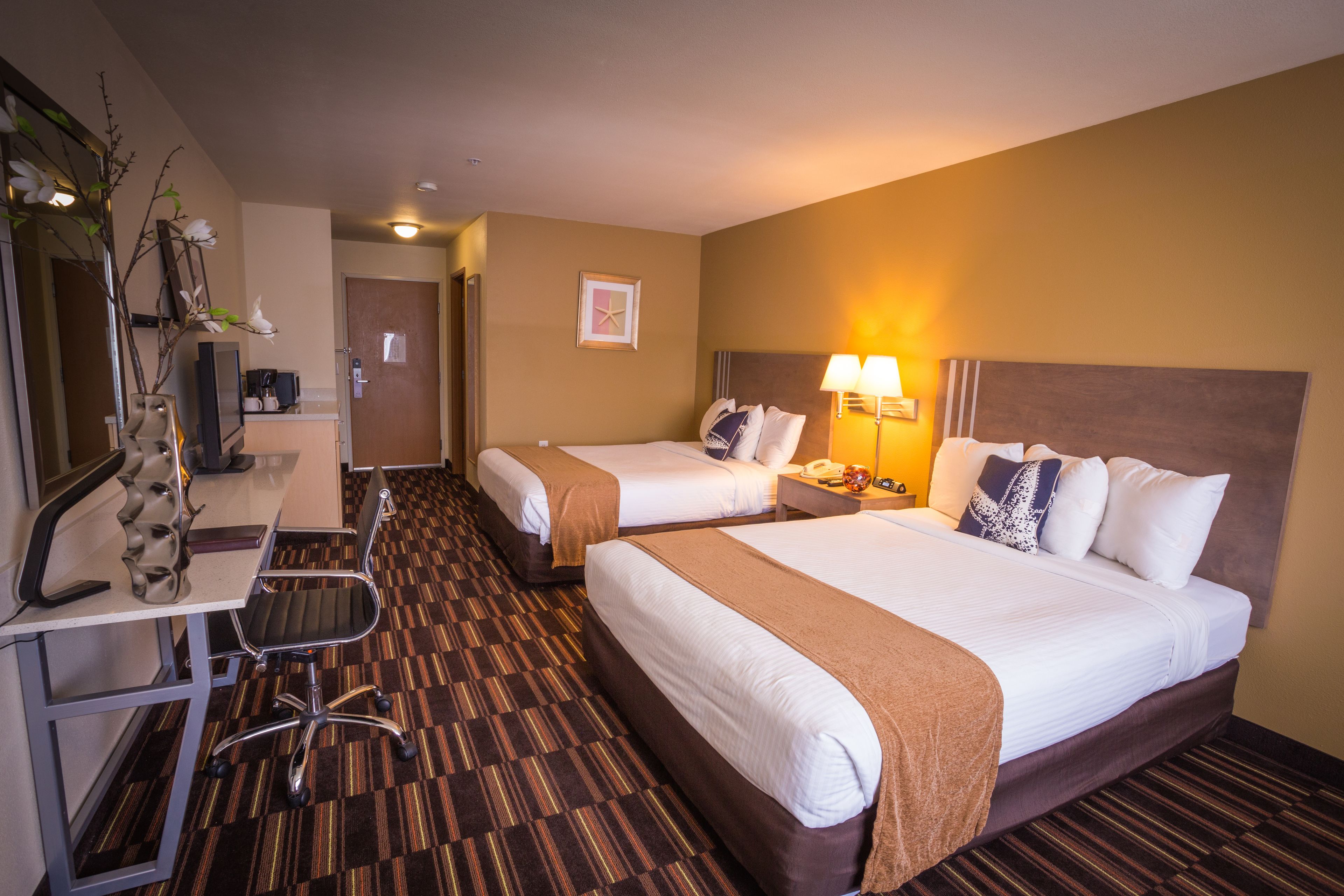 Ein Hotelzimmer mit zwei Betten, einem Schreibtisch mit Stuhl, einem Fernseher und einem Spiegel.