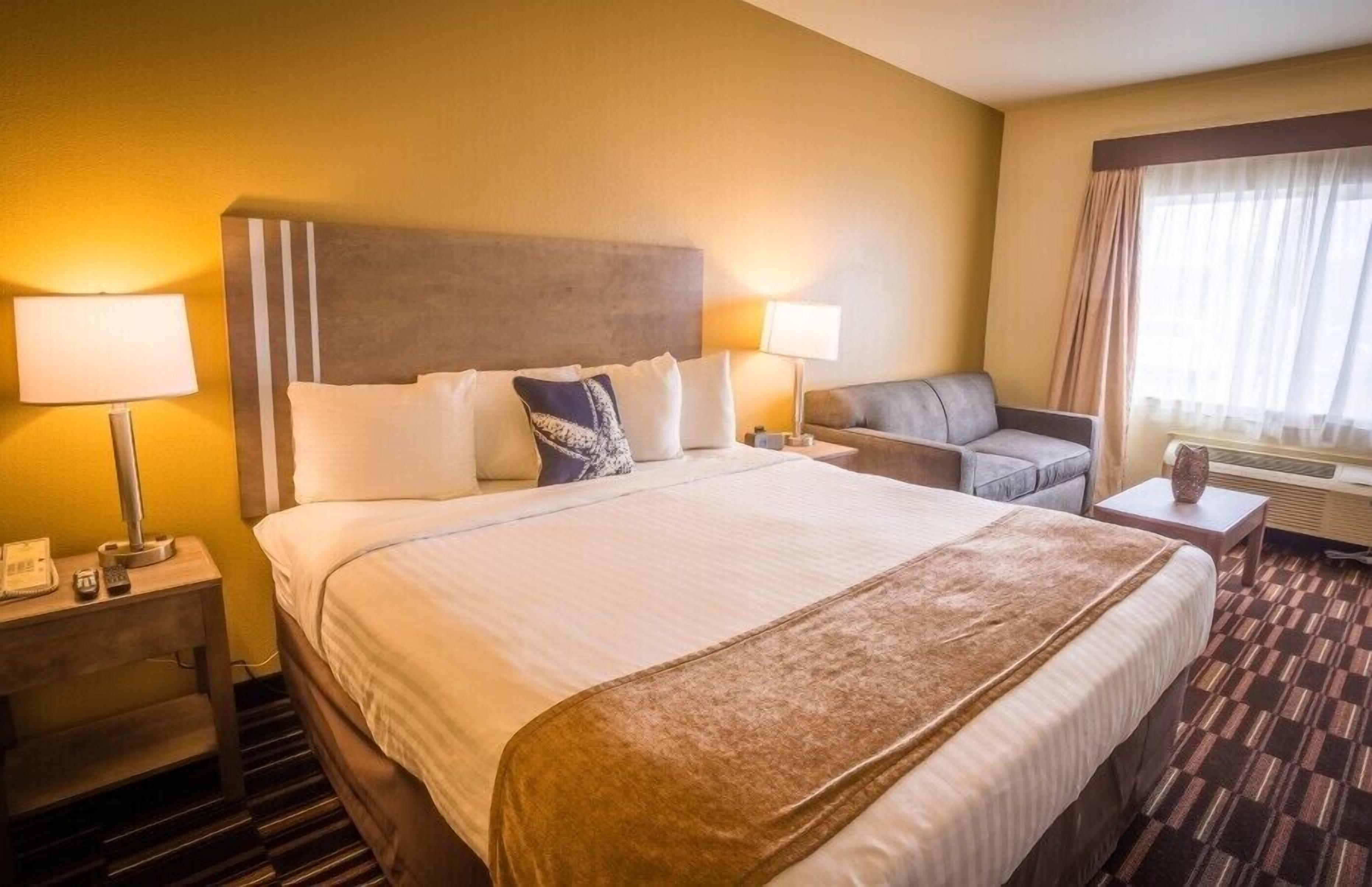 A hotel room with a large bed, two bedside tables, a sofa, and a window with curtains.