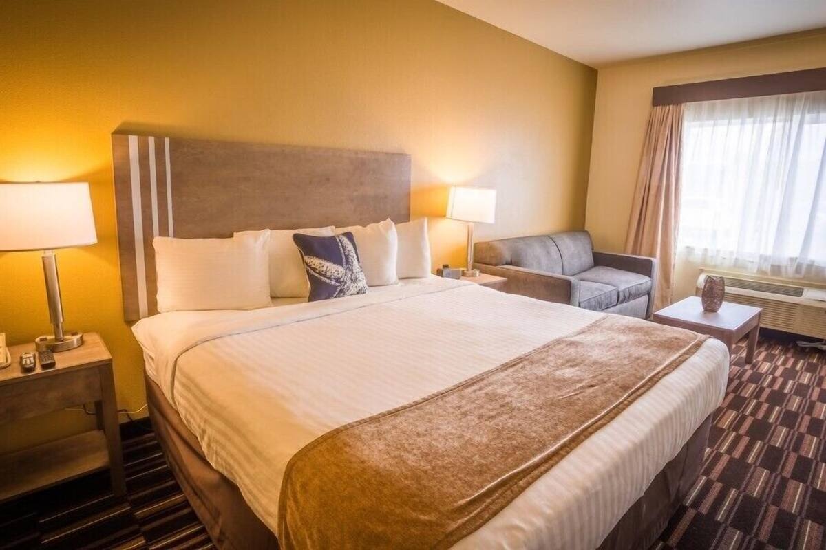 Ein Hotelzimmer mit einem großen Bett, zwei Nachttischen, einem Sofa und einem Fenster mit Vorhängen.