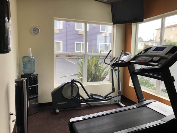 A gym with a treadmill, an elliptical, and a water dispenser.