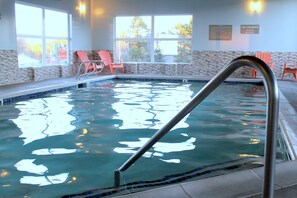 An indoor swimming pool with clear water, a metal pool ladder, and two red chairs near the window.