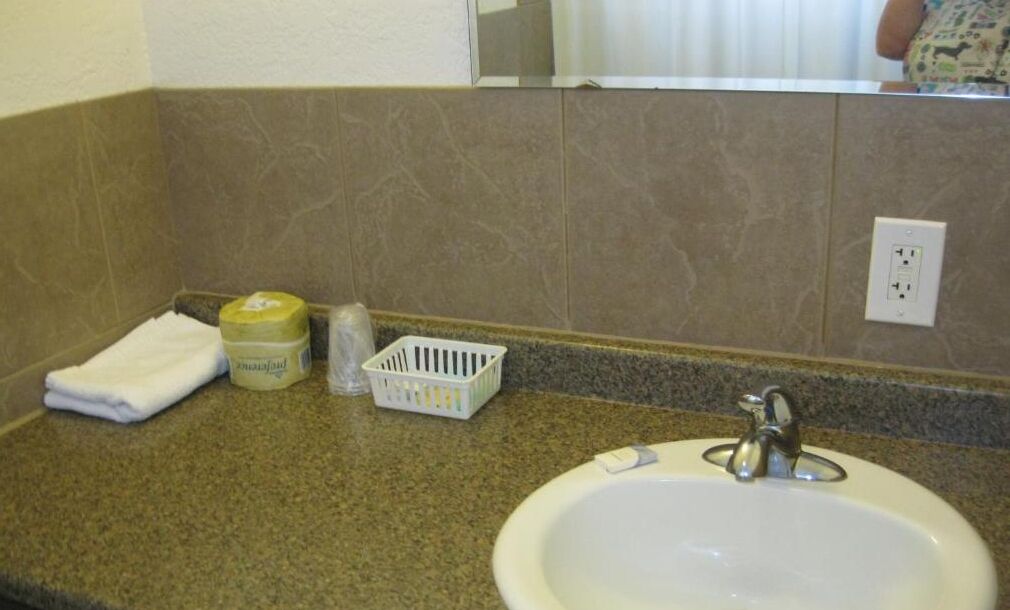 Een badkamer met een wastafel, een handdoek, een zeepdispenser en een klein mandje.