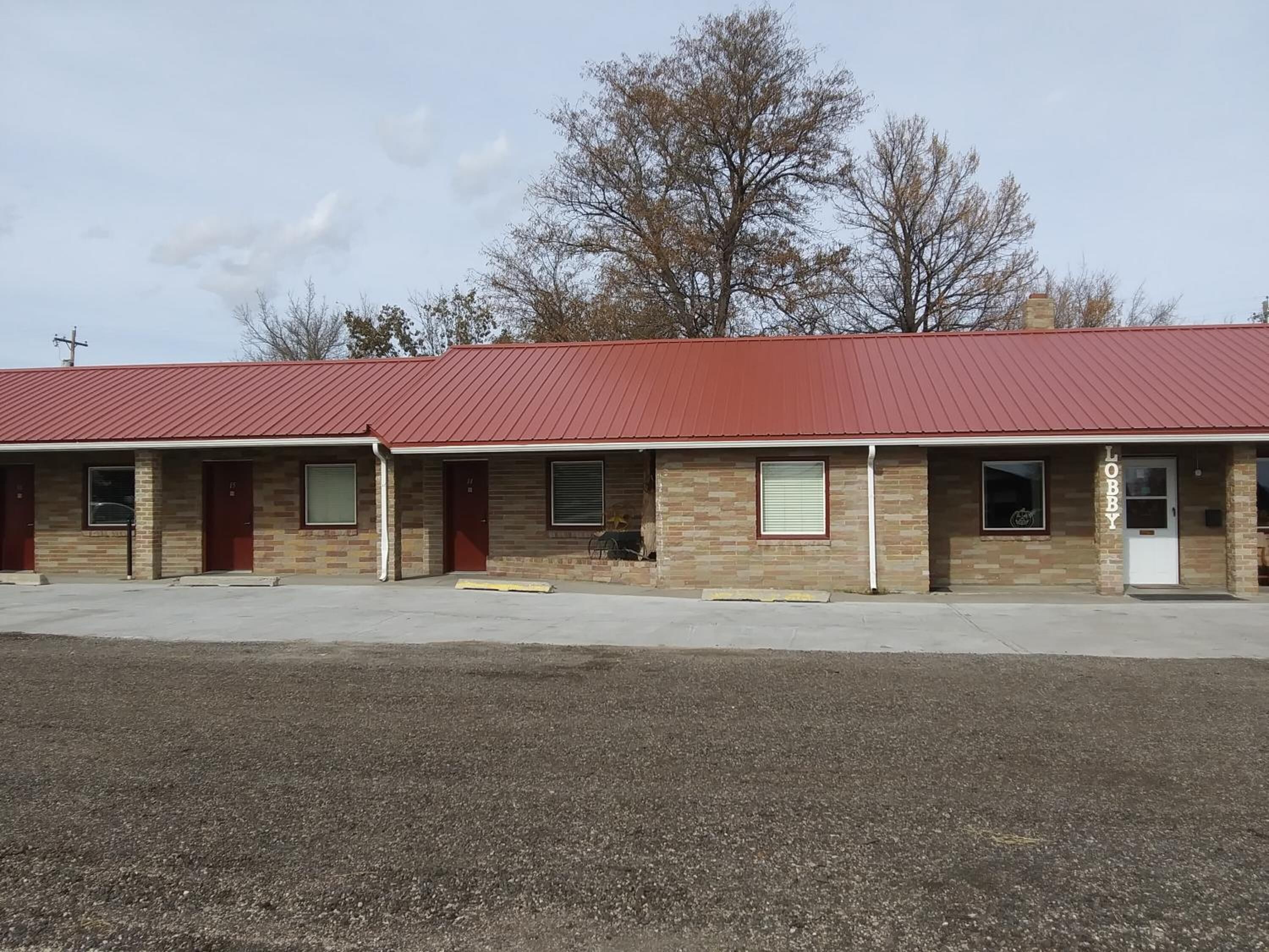 A motel with a red roof and brick exterior. It has multiple rooms with windows and doors.